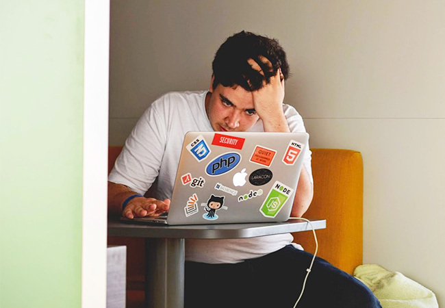 Ein junger Mann sitzt am Laptop und sieht verzweifelt aus, weil er möglicherweise online auf einen Betrug hereingefallen ist. Internetbetrug anzeigen – das sollte sein nächster Schritt sein. Bild: Unsplash/Tim Gouw